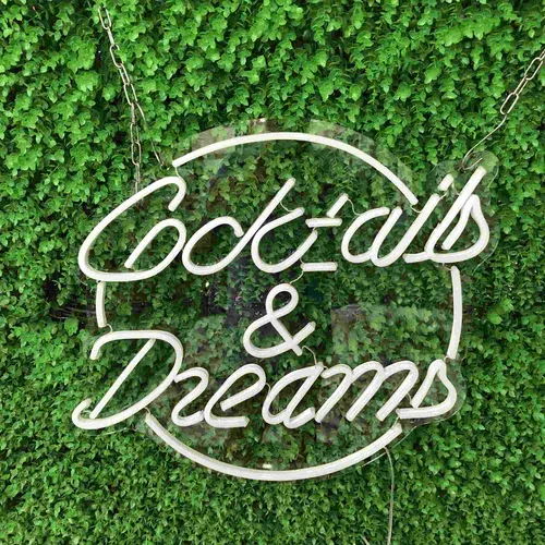 Green-wall bar interior with a white LED neon sign reading Cocktails and Dreams